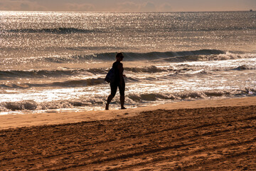 Fototapeta na wymiar Silueta de mujer paseando por la orilla de la playa con un brillante amanecer