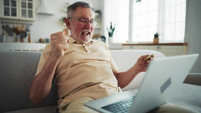 One man senior caucasian male with beard sit home in day with laptop computer making online purchase shopping buy stuff hold credit card pensioner enjoy his retirement. Older man with technology.