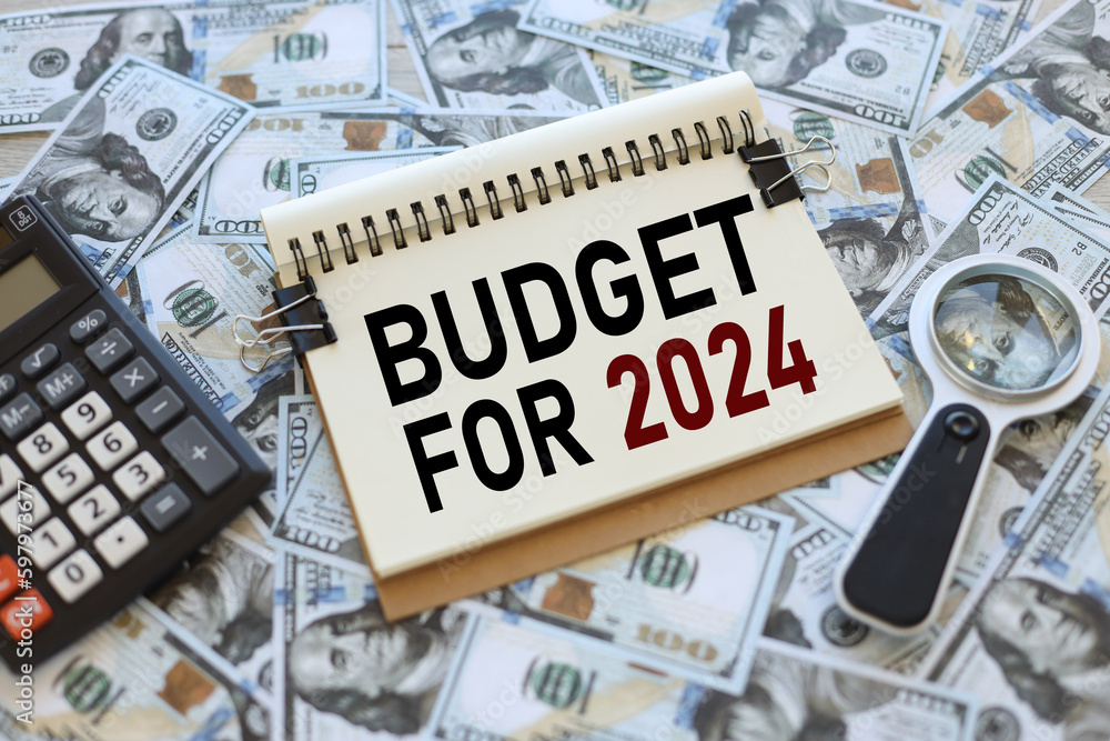Poster budget 2024. clip notepad. text in an open notepad. on scattered bills of money