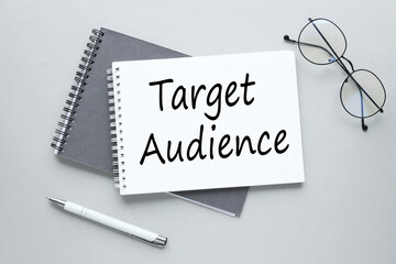 Target Audience open notepad with text.glasses and pen gray background.