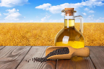 rapeseed oil in bottle with rape seeds in scoop on table and canola field as background