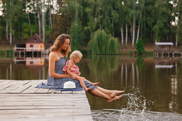 mother and daughter walk on the bridge by the water, girl in a hat on a wooden bridge, walk by the...