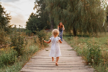 mother and daughter walk on the bridge by the water, girl in a hat on a wooden bridge, walk by the pond, pond, family near the lake


