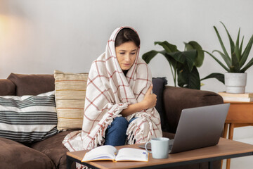 Sick young woman feel cold covered with blanket sitting at home on the couch forced to work. Flu...