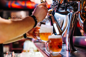 man bartender hand at beer tap pouring beer in glass in bar or pub