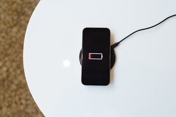 Charging mobile phone battery with wireless charging device in the table. Smartphone charging on a charging pad. Mobile phone near wireless charger Modern lifestyle technology concept.
