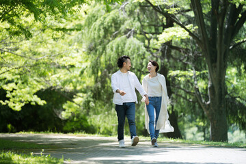 A couple walking hand in hand in fresh green in the light, gazing at each other, wide angle, with space for photocopying