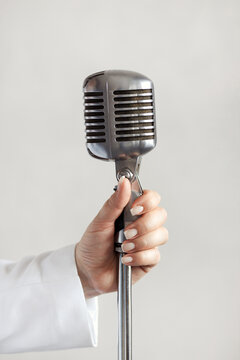Female hand holding a retro silver microphone on white wall background