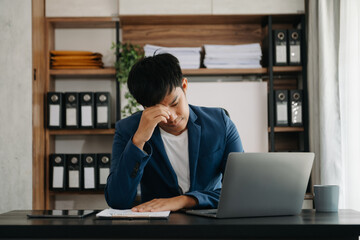 Frustrated young businessman working on a laptop computer sitting at his working place in office..