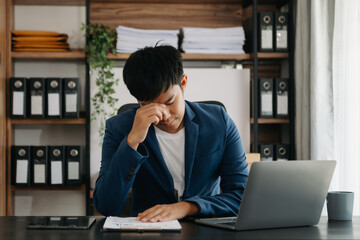 Frustrated young businessman working on a laptop computer sitting at his working place in office..