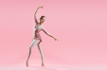 elegant young ballerina in pointe shoes dancing on a delicate pink background