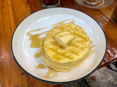 Stack of plain pancakes with butter and honey on a white plate