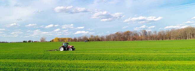 Panorama view large grassy farmland meadow field with working tractors rotary cutter trailer, colorful fall foliage cloud sky in South Lockport, Niagara County, New York, USA