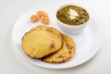 Sarso saag with makki roti served with jaggery in white plate isolated on white background, punjabi food