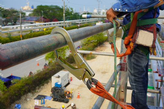Hook of safety harness on scaffolding pipe during working at heights in construction site, Chemical plant.