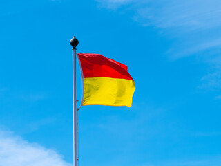 A red and yellow flag allowing swimming on the beach. One flag on a blue sky background.