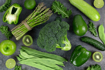 Healthy organic food: green vegetables and herbs on a dark background. Top view. Assorted green vegetables: broccoli, beans, avocado, apple, zucchini, kiwi on a gray background.