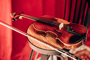 A wooden brown violin lies on a chair with a red curtain. Musical instrument for violinist