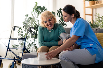 Senior woman getting her blood pressure measured during regular home care visit. Young supportive...