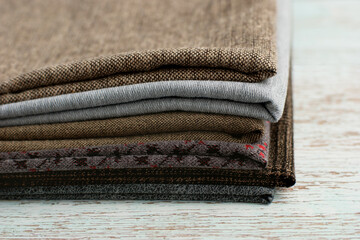 A stack of fabric on a wooden table. Different fabric for sewing clothes and design close-up....