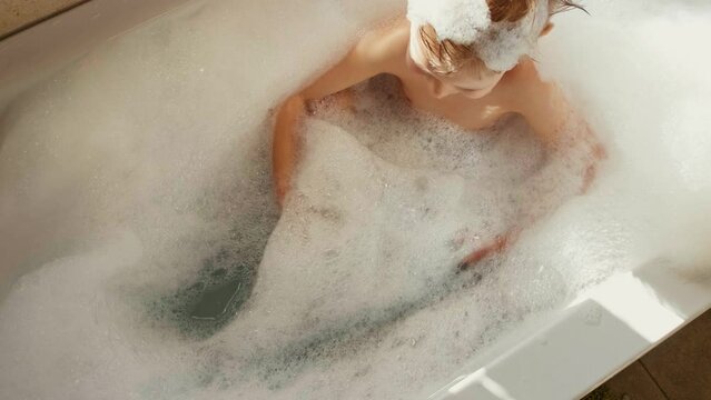 A little boy bathes in a bath. Bath games. Daily care. Shampoo and bath foam. The child bathes. boy playing with dinosaurs