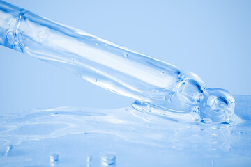 Transparent cosmetic gel flowing from the dropper and smeared on the background. On a blue background. Hyaluronic acid, toner, toner, gel, cream. Cosmetics.