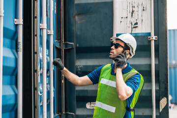 Young construction worker standing in container warehouse in construction process and using smart phone. It’s break time.