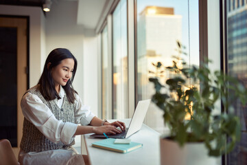Young smiling Asian business woman employee or student working on laptop in corporate office. Happy professional businesswoman marketing manager using computer technology sitting at Generative AI