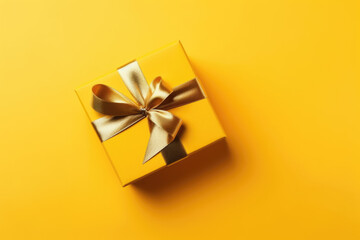 Gift box with golden satin ribbon and bow on yellow background. Holiday gift with copy space. Birthday or Christmas present, flat lay, top view. Christmas giftbox concept