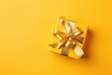 Gift box with golden satin ribbon and bow on yellow background. Holiday gift with copy space. Birthday or Christmas present, flat lay, top view. Christmas giftbox concept