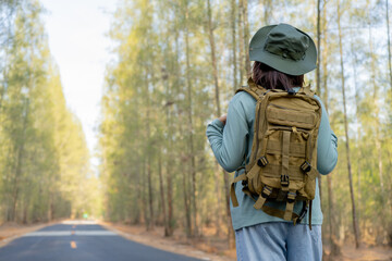 Young Asian girl with a backpack and hat hiking in the mountains during the summer season, a traveler walking in the forest. Travel, adventure, and journey concept.