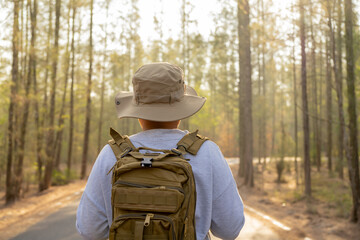 Fototapeta na wymiar Young Asian man with a backpack and hat hiking in the mountains during the summer season, a traveler walking in the forest. Travel, adventure, and journey concept.