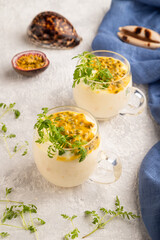 Yogurt with passionfruit and marigold microgreen in glass on gray. Side view, close up.