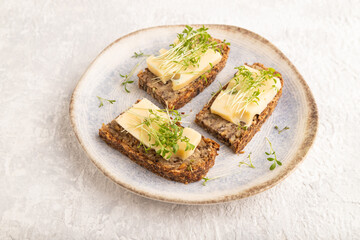 Grain bread sandwiches with cheese and watercress microgreen on gray concrete, side view, close up.