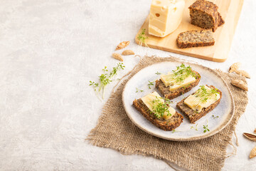 Grain bread sandwiches with cheese and watercress microgreen on gray concrete, side view, copy space.