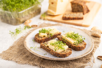 Grain bread sandwiches with cheese and watercress microgreen on gray concrete, side view, selective focus.