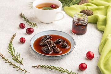 Pine cone jam with herbal tea on gray concrete, side view, selective focus.