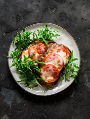 Hot sandwiches with mozzarella, tomatoes and arugula on a dark background, top view