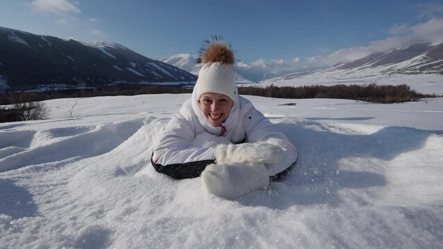 Young happy woman lying on snow on mountains background, slow motion