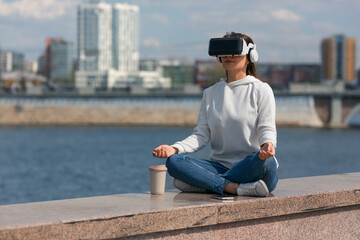 Fototapeta na wymiar Young woman meditating in vr glasses on embankment.