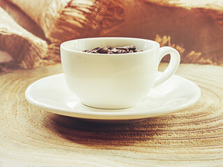 White cup with coffee beans, on a wooden background. Selective focus.