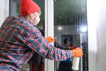 Spraying the drug against harmful mold in the house on the windows, the woman removes the fungus on...