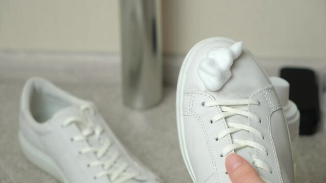 Applying cleaning foam from the bottle to white leather women's sneakers. Care for leather shoes, surface whitening
