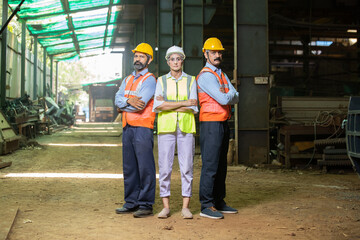 Team of happy confident indian engineers wearing safety hard hat and vest standing at industrial...