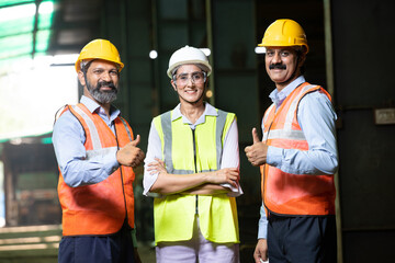 Team of happy confident indian engineers wearing safety hard hat and vest standing at industrial...