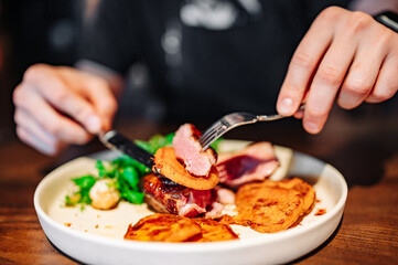 man with a knife and fork cuts grilled duck meat