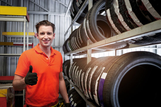 Auto mechanic handsome man giving thumb up during checking wheel tires at vehicle repair service shop, man working in garage, car service technician checking warehouse stock at automobile car service.