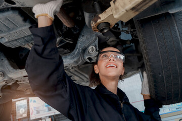 Beautiful female auto mechanic checking wheel tires in garage, car service technician woman repairing customer car at automobile service, inspecting vehicle underbody and suspension engine system.