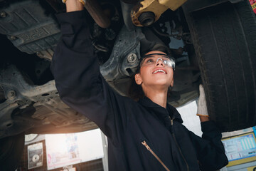 Beautiful female auto mechanic checking wheel tires in garage, car service technician woman repairing customer car at automobile service, inspecting vehicle underbody and suspension engine system.