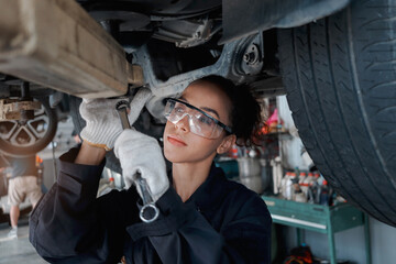 Beautiful female auto mechanic checking wheel tires in garage, car service technician woman repairing customer car at automobile service, inspecting vehicle underbody and suspension engine system.